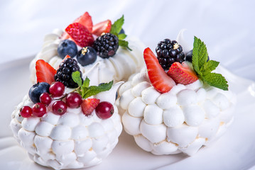 Delicate white meringues with fresh berries on the plate. Dessert Pavlova close-up. White background. Wedding cake.