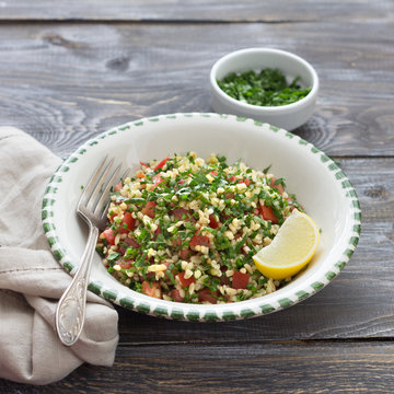 Tabbouleh, traditional arabic salad of bulgur, parsley and tomatoes on a wooden table. Delicious diet food