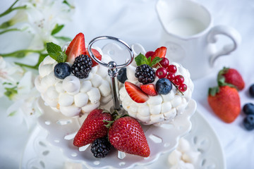 Delicate white meringues with fresh berries on the plate on white background. Dessert Pavlova. Wedding cake.