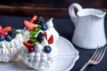 Delicate white meringues with fresh berries on the plate. Dessert Pavlova. Dark background. Wedding cake.