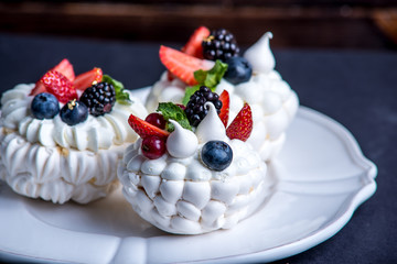 Delicate white meringues with fresh berries on the plate. Dessert Pavlova. Dark background. Wedding cake.