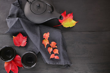 Autumn tea. Autumn mood.black  teapot and two cups in Asian style, black linen napkin and bright autumn leaves on a black wooden background.Autumn season. Autumn time