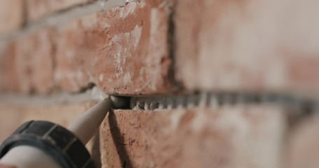 Slow motion closeup of worker filling seam between bricks with mortar from sealant gun