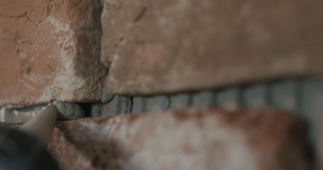 Slow motion closeup of worker filling seam between bricks with mortar from sealant gun