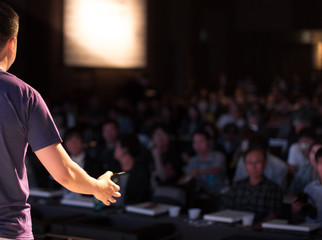 Presenter Speaking to Audience People in Conference Hall Auditorium. Presentation Stage. Blurred...