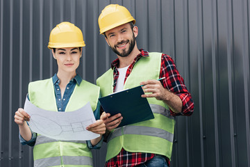 architects in safety vests and hardhats working with blueprint and clipboard on roof