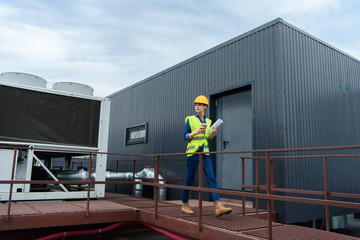 professional female engineer in safety vest and hardhat with blueprint on coffee break on roof