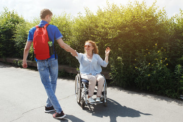 Woman in a wheelchair with her boyfriend strolling in the city summer park.