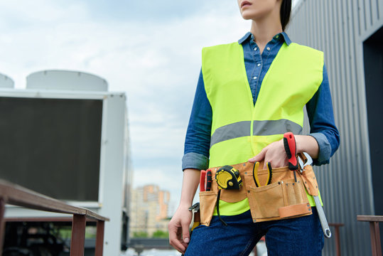 cropped view of female engineer with tool belt in safety vest