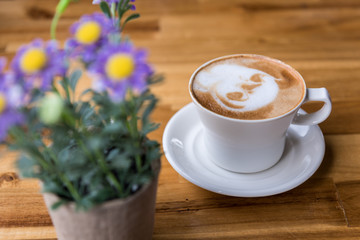 Latte art coffee cup with purple flowers vase on wooden table