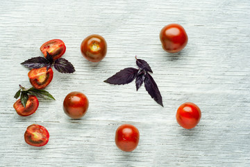Fresh red cherry tomatoes with basil on a rustic wooden background, selective focus.