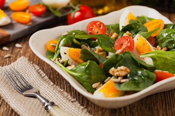 Delicious salad of fresh spinach, boiled egg, tomatoes, nuts and sunflower seeds