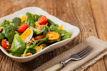 Delicious salad of fresh spinach, boiled egg, tomatoes, nuts and sunflower seeds