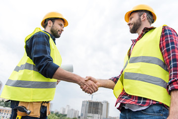 two engineers in safety vests and helmets shaking hands on roof