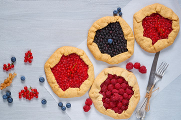 Various berries galette with knife and fork on the gray background. Vegetarian healthy tarts with fresh blueberries, raspberries, red currants. Delicious dessert. Top view  with copy space for text