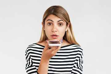 People, electronic gadgets and modern technology concept. Picture of serious attractive young woman recording voice message using wireless high speed internet connection on generic mobile phone