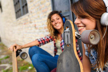 Obraz na płótnie Canvas Skate girls sitting in the street hanging out listening music with earphones and smartphone