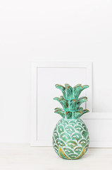 Wooden empty frames for a photo and a wooden emerald pineapple on a background of a white wall. Blank paper frames, modern home decor mock-up. Interior background.