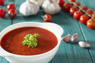 Creamy tomato soup with parsley and garlic on a blue kitchen table 