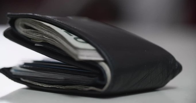 pulling focus on a folded and very used wallet with cards and cash inside on a table with a blurry background
