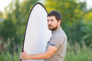 Photographer's assistant holding white reflector outdoors, summer day.