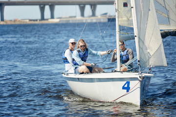 Fototapeta premium Serious modern men riding on sailboat: young professional yachtsman pulling sail with rope while handling sail boat by means of wind