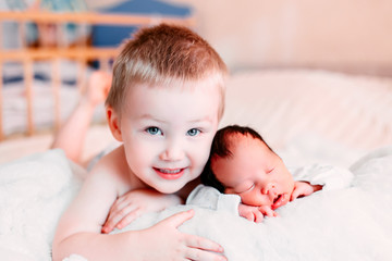 Elder brother and newborn baby sister lying on bed at home