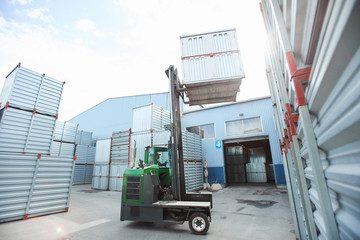 Modern powerful forklift truck lifting metal container while stacking it on others in outdoor...