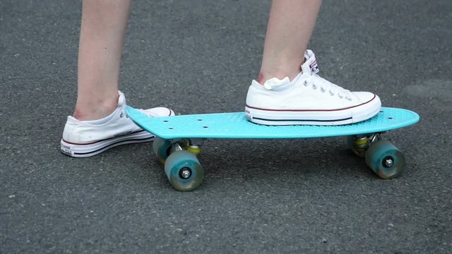 skateboarding, leisure, extreme sport and people concept - teenage girl legs riding short modern cruiser skateboard on road