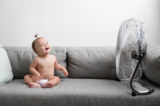 Laughing baby girl sitting on sofa next to fan