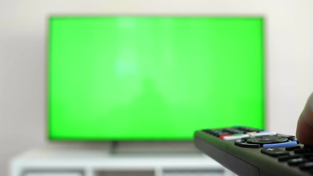 Watching tv with green screen at home interior. Push buttons on remote. Changing channels on television