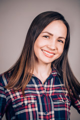 Fototapeta premium Happy cheerful young woman wearing plaid shirt looking at camera with joyful and charming smile. student girl, close-up portrait on grey background