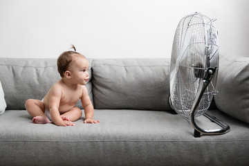 Baby girl sitting on couch next to fan