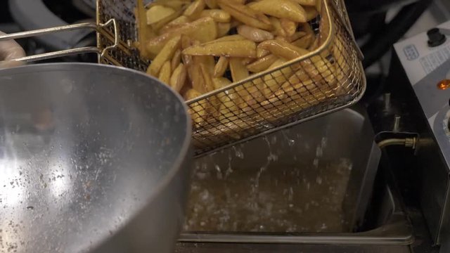  The cook in cooks the potatoes in the deep-fryer. Fried, cooking process, fries