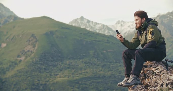 Young adventurer chatting on phone in mountains. climber on top of mountain. social networks concept 4k