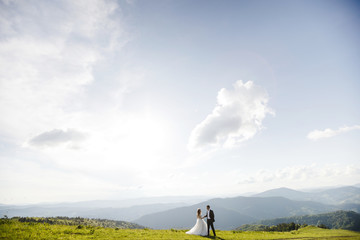 Naklejka na ściany i meble Romantic couple newlyweds posing at sunset on a background of mountains.