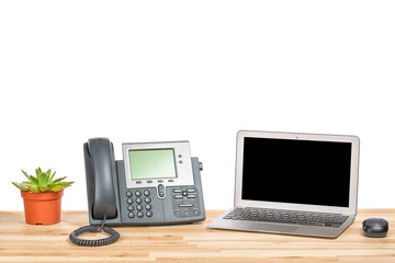 Conceptual workspace or business office concept. Laptop computer with modern IP phone, plant in a pot and computer mouse on light wooden table. Isolated background.