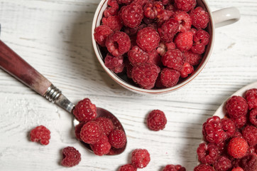 Ripe sweet raspberries in bowl, in cup and in saucer on wooden table.