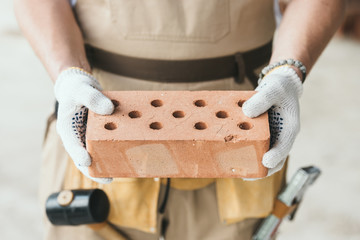 cropped image of builder in protective gloves holding brick