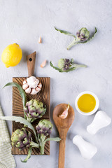 Fresh ripe green artichokes on cutting board ready to cook and ingredients garlic, lemon and olive oil