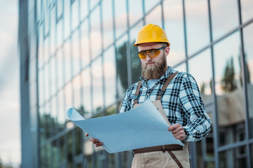 construction worker in protective googles and hardhat looking at blueprint