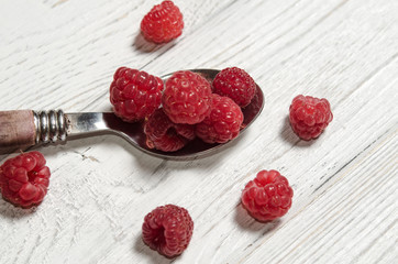Ripe sweet raspberries in spoon on wooden table.