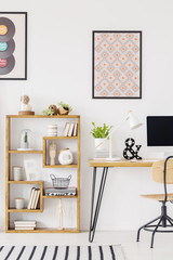 Poster above wooden desk with plant and computer desktop in home office interior. Real photo