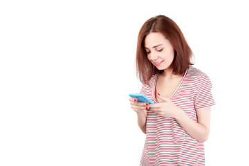 Closeup photo of casually-dressed European girl standing isolated on gray background looking attentively at screen of cellphone, browsing web pages and smiling nicely while chatting with friends.
