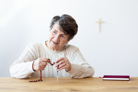 Smiling religious grandmother with rosary sitting at table with bible