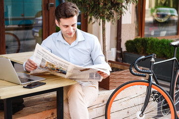 Smiling young stylish man in shirt reading newspaper