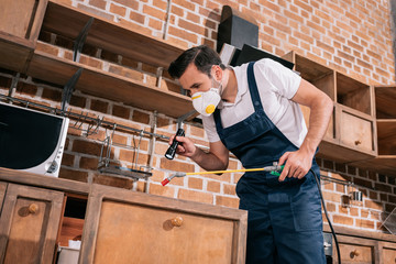 pest control worker spraying pesticides in kitchen and using flashlight