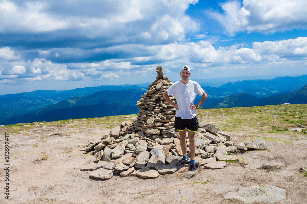 Wall mural man hiker relaxing on top of hill and admiring beautiful mountain valley view in summer day