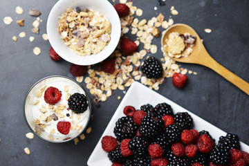 Muesli cereals, yogurt and fresh berries on dark background, preparing a healthy and delicious breakfast with natural ingredients
