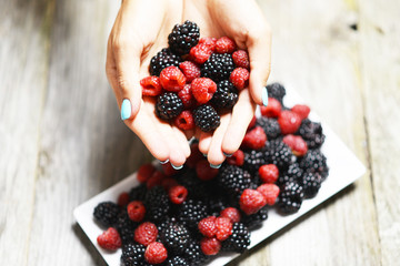 Woman hand holding red ripe raspberries and blackberries, fresh fruits for a healthy lifestyle 
